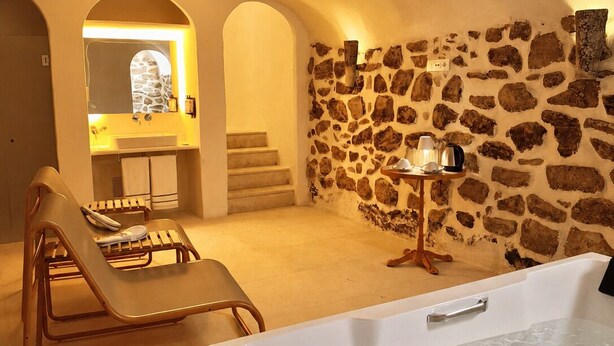 A spa area with a bathtub, lounge chairs, a stone wall, and a small table with a lamp. - Hotel Casa Treviño (Campo de Criptana)