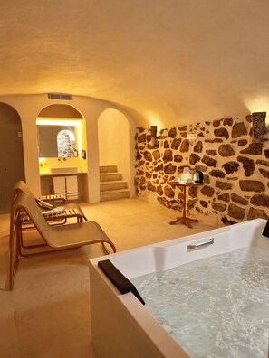 A spa area with a bathtub, lounge chairs, a stone wall, and a small table with a lamp. - Hotel Casa Treviño (Campo de Criptana)