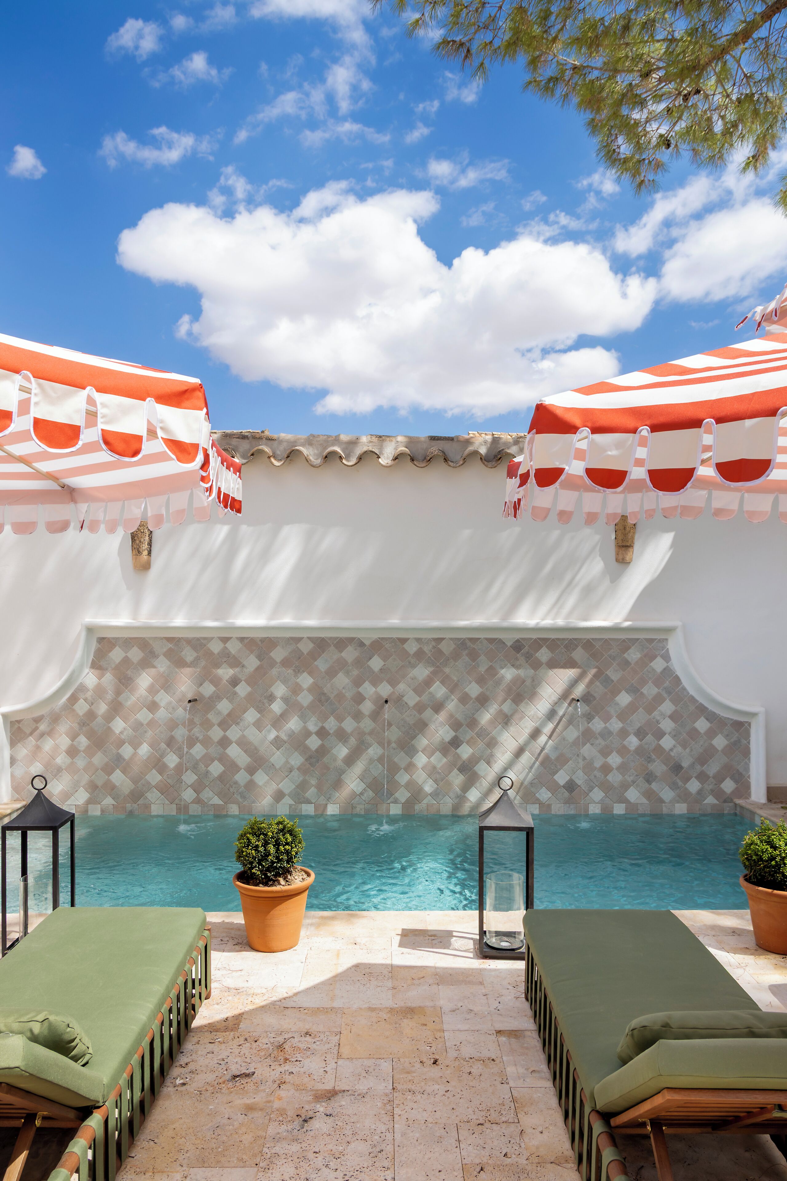 Un área junto a la piscina con dos sillas de descanso, una pared de azulejos y un cielo azul despejado.