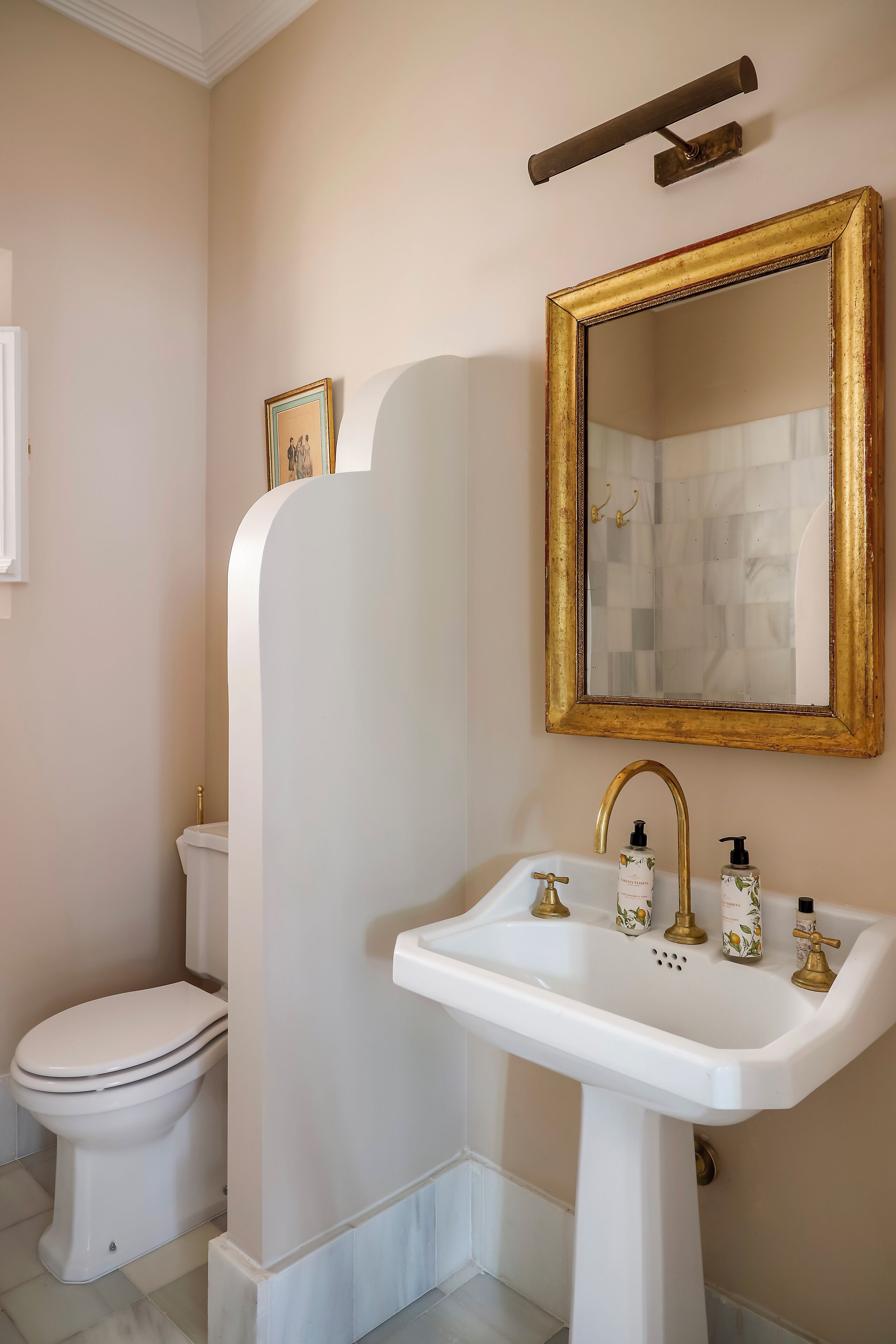 Un baño con un lavabo blanco, grifos dorados, un espejo con marco dorado y un inodoro blanco.