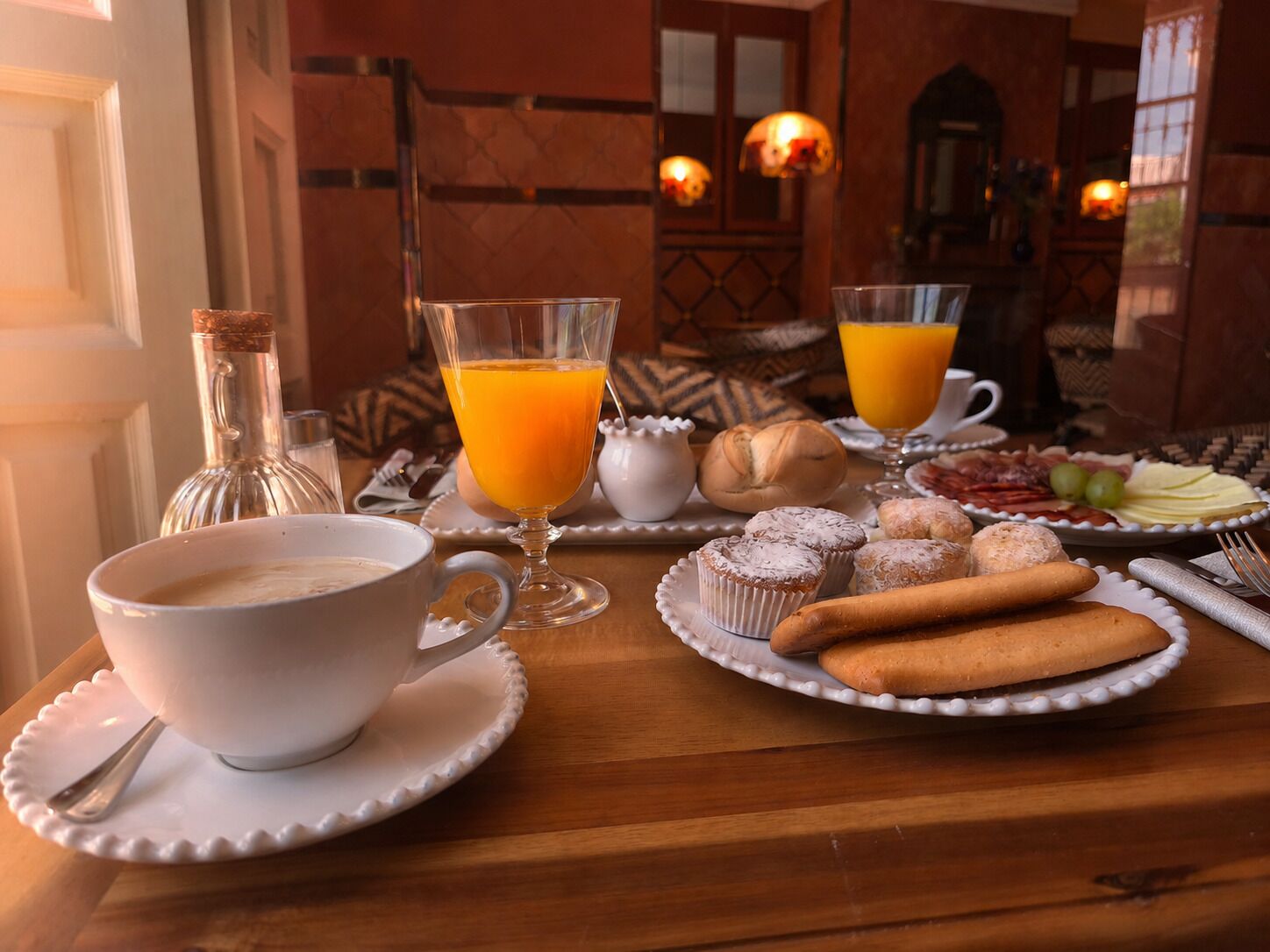 Mesa de café da manhã com xícara de café, copo de suco de laranja, pães e uma garrafa de água.