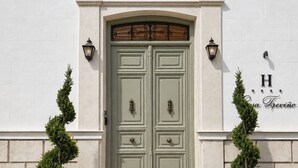 A double door with a decorative arch above it, flanked by two wall-mounted lanterns and two potted evergreen plants. - Hotel Casa Treviño (Campo de Criptana)