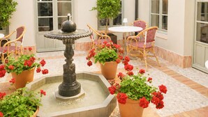 A courtyard with a fountain, potted plants, and wicker chairs. - Hotel Casa Treviño (Campo de Criptana)