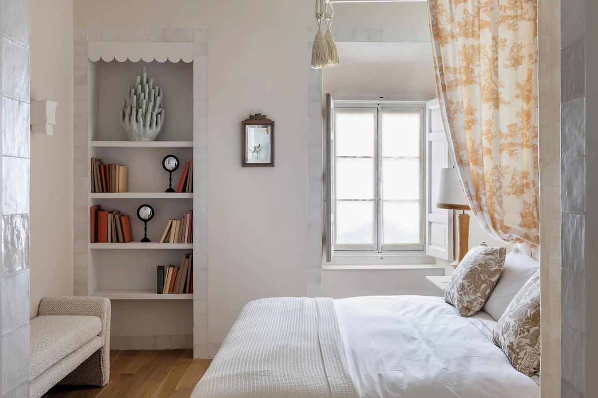 Ein Schlafzimmer mit einem Bett, einem Bücherregal, einem Fenster und einer Pendelleuchte.