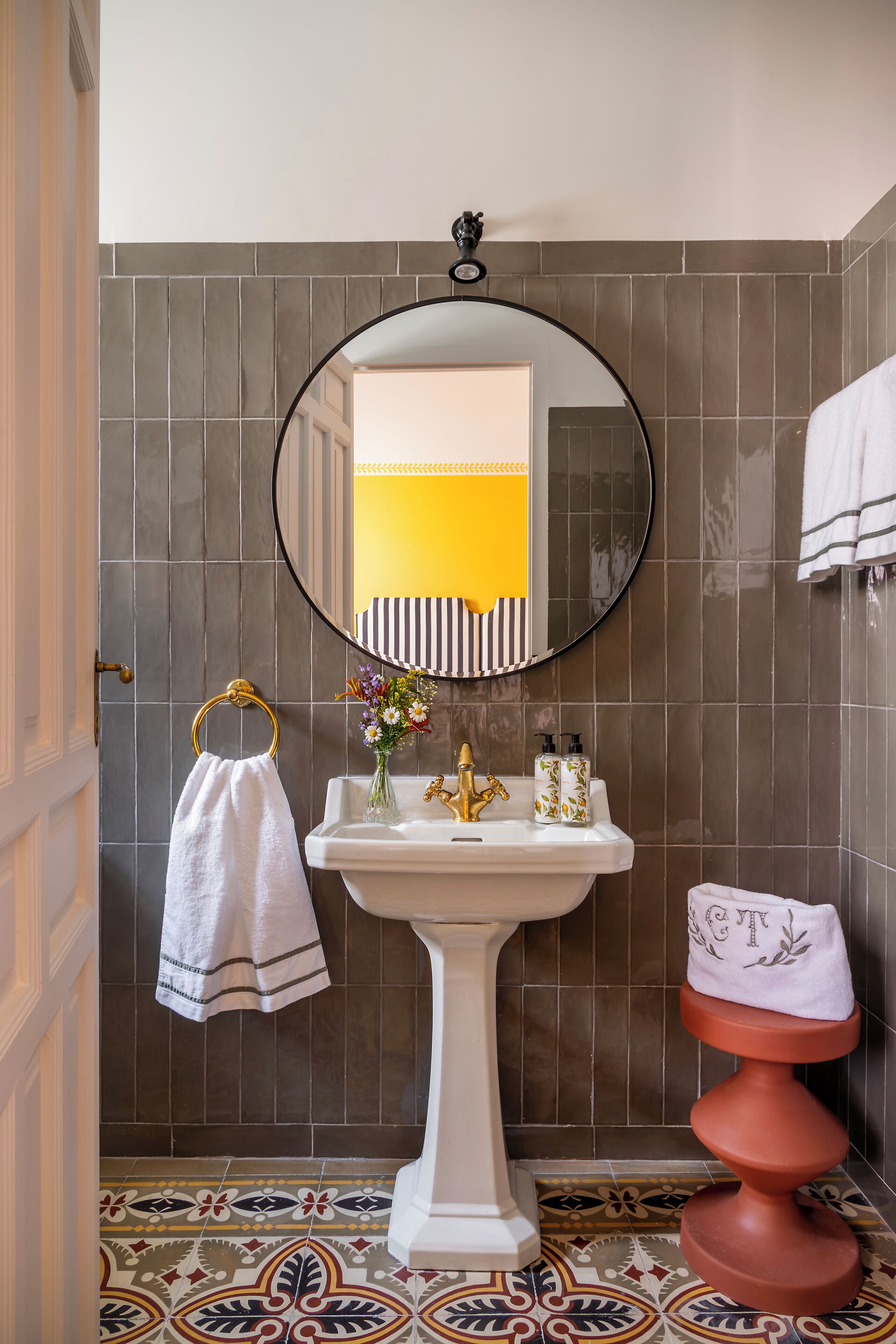 A bathroom with a white pedestal sink, a round mirror, a towel rack, and a toilet with a towel on top.