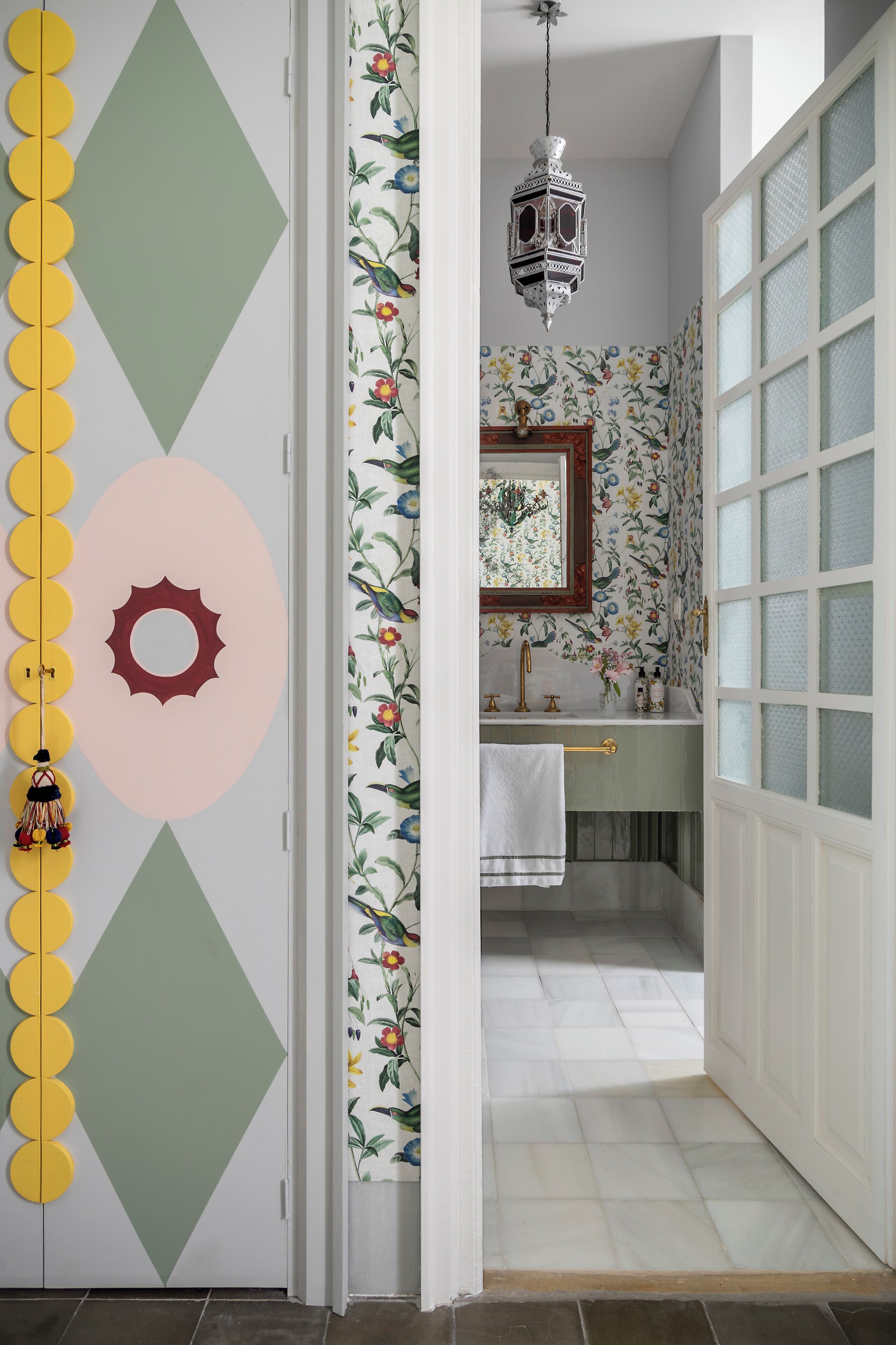 A bathroom with floral wallpaper, a sink, a mirror, and a hanging lantern.