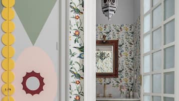 A bathroom with floral wallpaper, a sink, a mirror, and a hanging lantern.