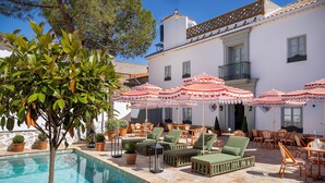 A poolside area with lounge chairs, umbrellas, and potted plants. - Hotel Casa Treviño (Campo de Criptana)