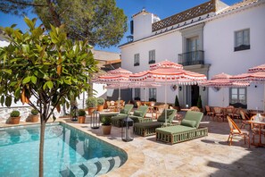 Zona de piscina con sillones, sombrillas y plantas en macetas.