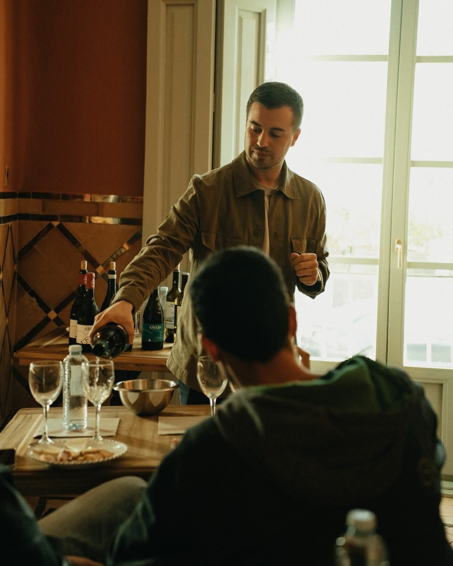 A person pouring wine into a glass at a table with wine bottles and glasses.
