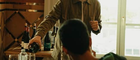 Una persona sirve vino en una copa sobre una mesa con botellas y copas de vino.