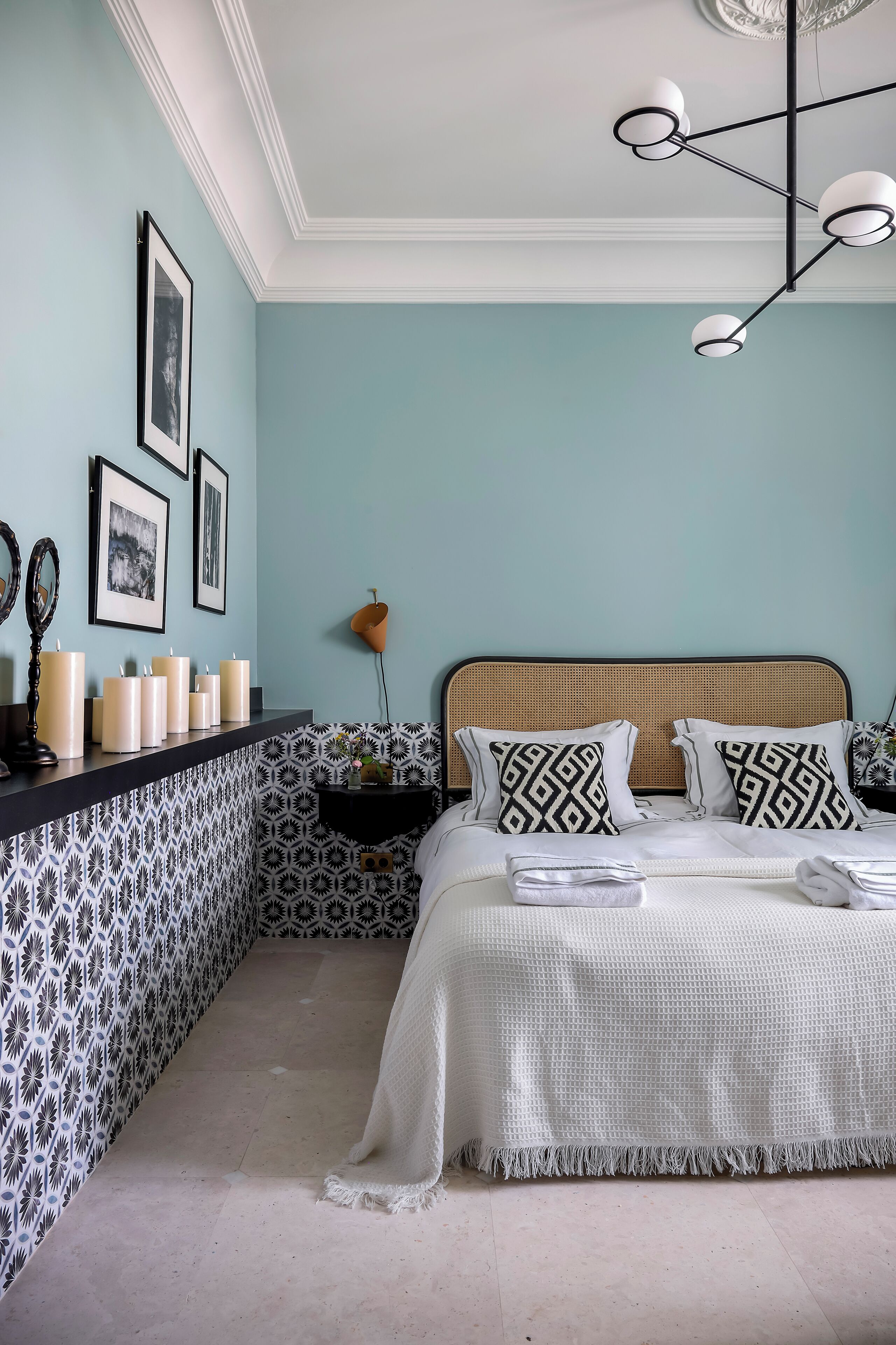 Un dormitorio con cama, mesita de noche, espejo en la pared y cuadros enmarcados.