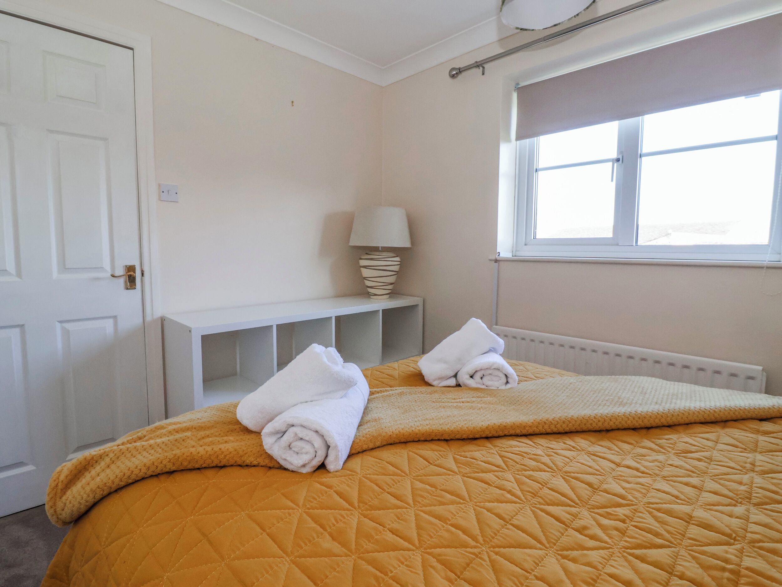 Ein Hotelzimmer mit Bett, Fenster, Lampe und Ablagefläche mit einem gefalteten Handtuch.