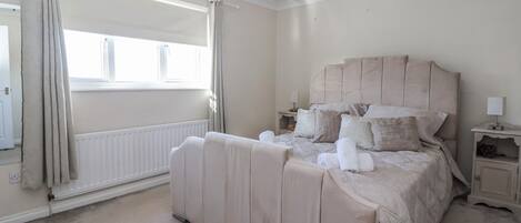 A bedroom with a large bed, a nightstand, a lamp, a radiator, and a window with curtains.