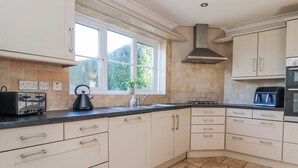 A modern kitchen with white cabinets, a gas stove, a toaster, and a window with a view of greenery. - Thorntons House (Northallerton)