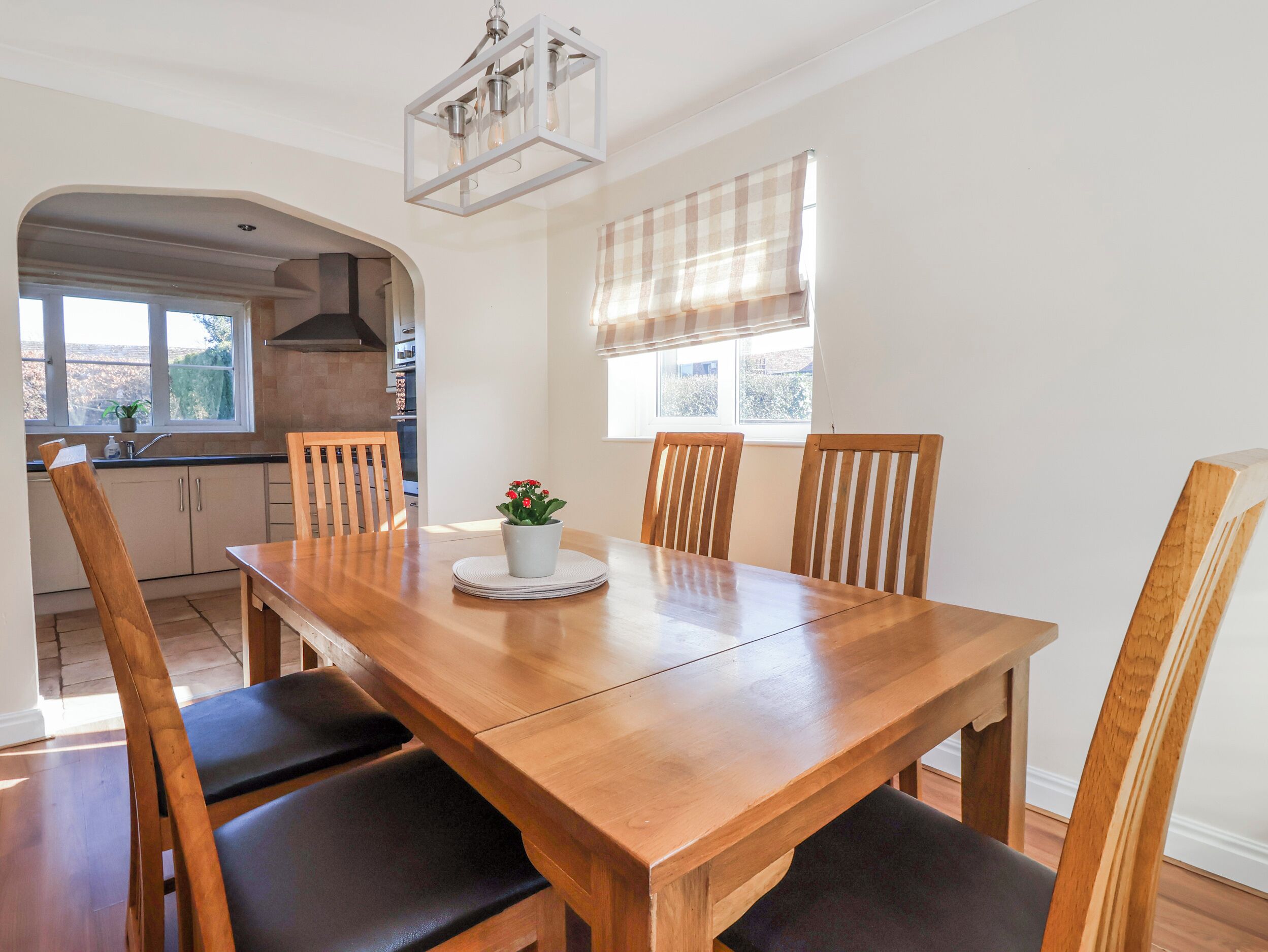 A dining area with a wooden table, four chairs, a potted plant, and a window with blinds.