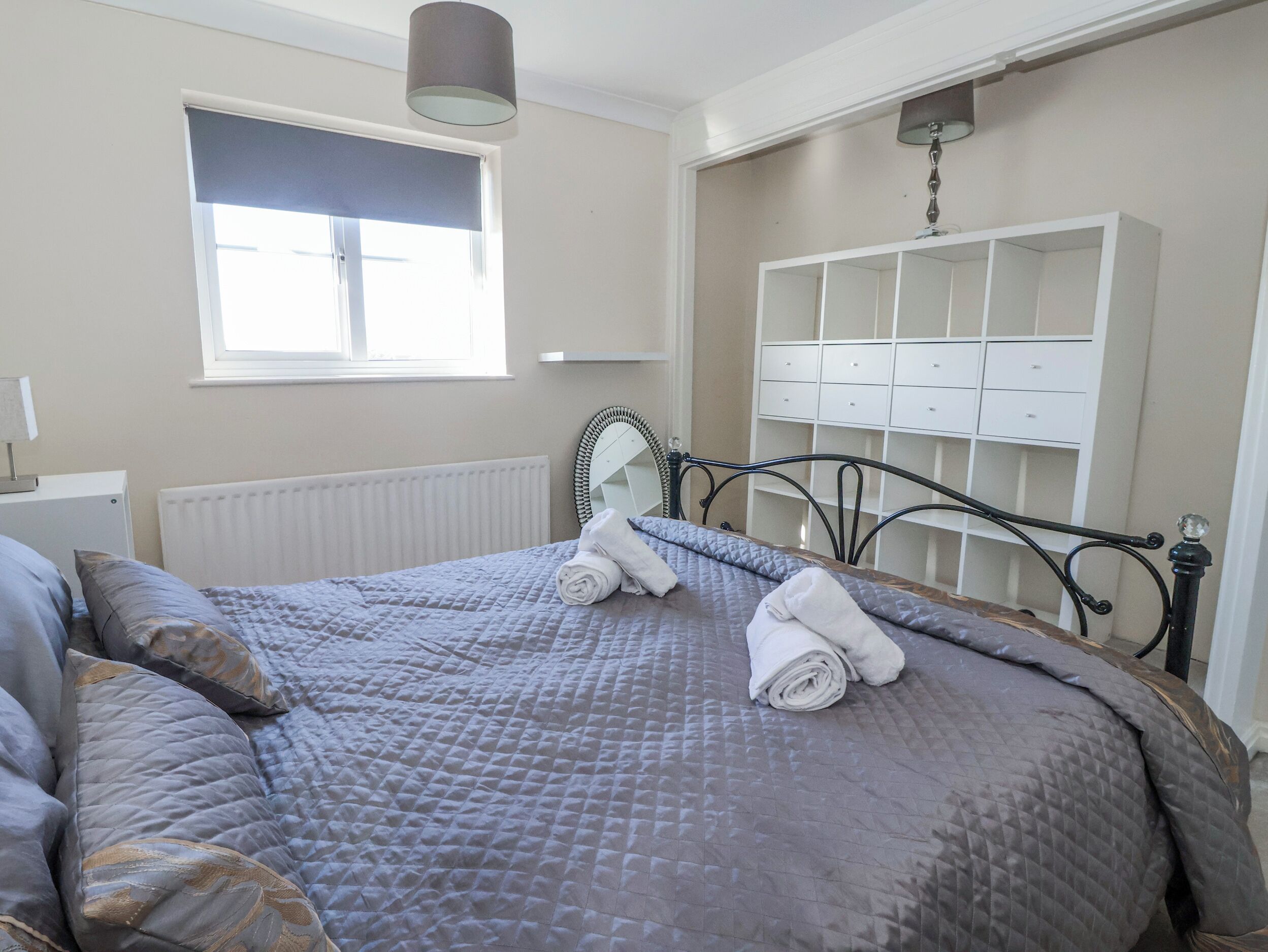A neatly made bed with a quilted blanket, a bedside lamp, and a window with blinds.