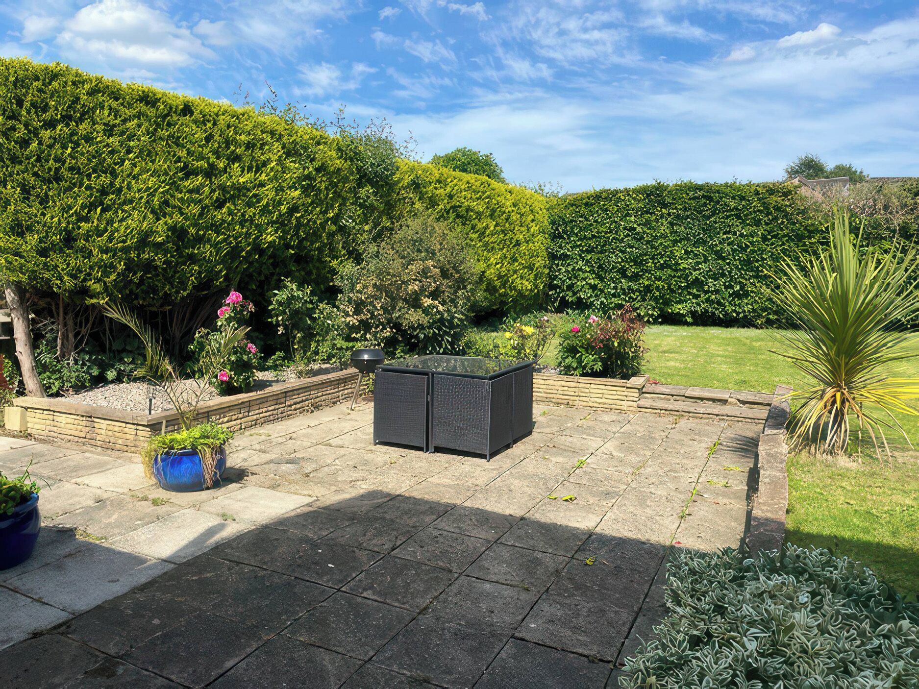 A garden patio with a seating area, a grill, and various plants.