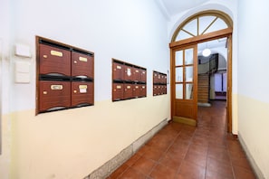 Un couloir avec des boîtes aux lettres en bois, un sol carrelé et une porte en bois donnant sur un escalier.