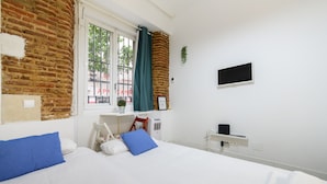 A hotel room with a brick wall, a bed with white and blue bedding, a desk with a chair, a TV, and a window with curtains. - M Piz401 Acogedor Estudio en el Centro de Madrid (Madrid)