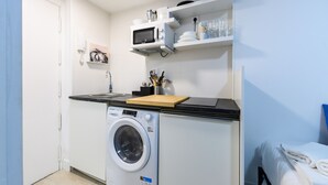 A compact kitchen with a washing machine, a microwave, and a small countertop. - M Piz401 Acogedor Estudio en el Centro de Madrid (Madrid)
