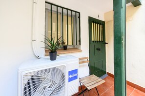 A white air conditioning unit with a Haier logo, a potted plant, a wooden chair, and a green door with a window above it. - M Svf1304 Acogedor Estudio en Centro de Madrid (Madrid)