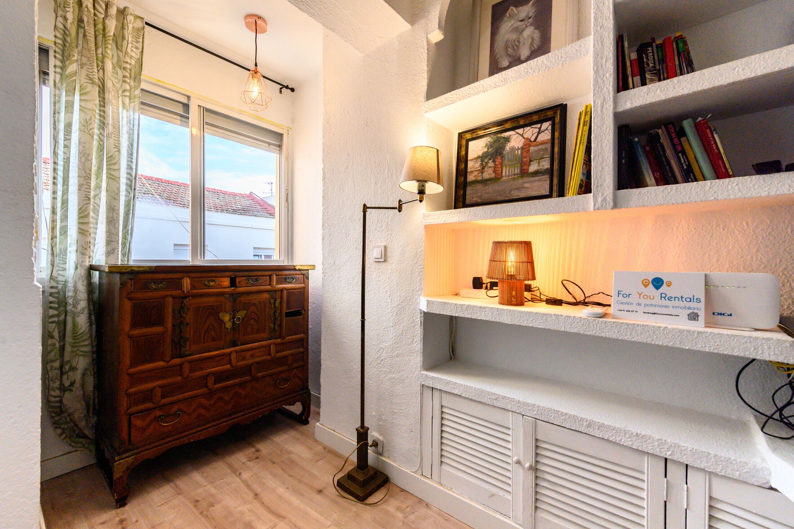 A room with a wooden dresser, a lamp, a bookshelf with books, and a sign for rentals.