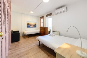 A bedroom with two beds, a dresser, a desk with a lamp, a painting on the wall, and an air conditioning unit. - M Por183d Amplio Piso 2 Dormitorios en La Latina (Madrid)