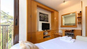 Hotelkamer met een bed, een televisie, een bureau met stoel, een spiegel en uitzicht op bomen.