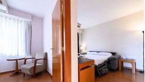 A compact hotel room with a bed, bedside table, lamp, chair, and a small desk. - M Mle16a2320 Amplio Piso 1 Dormitorio en Chamart (Madrid)