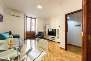 A living room with a glass table, chairs, a sofa, a TV, and a door leading to another room. - M May613 Piso de 1 Dormitorio en Pleno Centro de (Madrid)