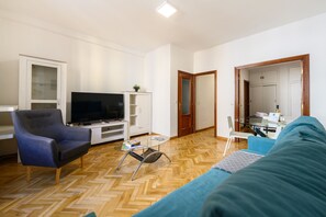A living room with a sofa, a television, a glass coffee table, and a wooden herringbone floor. - M May613 Piso de 1 Dormitorio en Pleno Centro de (Madrid)