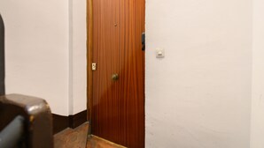 A wooden door with a brass handle and a keyhole, a light switch, and a dark-colored object on the floor. - M May613 Piso de 1 Dormitorio en Pleno Centro de (Madrid)