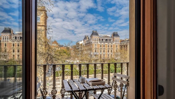 Varanda com mesa e cadeiras, vista para edifícios históricos e uma torre.
