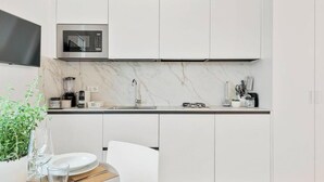 Una cocina moderna con armarios blancos, microondas integrado, salpicadero de mármol y un comedor con mesa para dos.