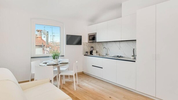 Una cocina compacta con gabinetes blancos, un protector contra salpicaduras de mármol y un microondas integrado.