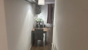 A narrow hallway with a wooden floor, a radiator on the right, a table with chairs, and a vase of flowers in the background. - Spacious studio flat in London (London)