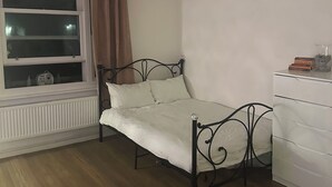 A bedroom with a bed, a radiator, a window with curtains, a ceiling fan, and a white dresser. - Spacious studio flat in London (London)