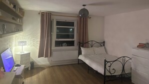 A bedroom with a bed, a bedside table, a lamp, a radiator, and a window with curtains. - Spacious studio flat in London (London)