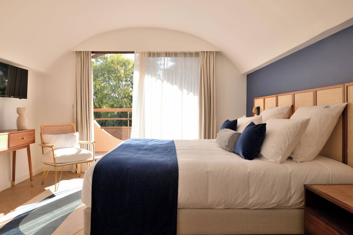 Ein Hotelzimmer mit einem großen Bett, einem Schreibtisch, einem Sessel und einem Fernseher an der Wand.