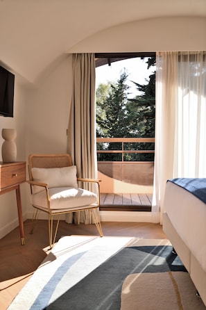 Une chambre avec une chaise en bois, un lit, une table de chevet et une vue sur l’extérieur grâce à un balcon.