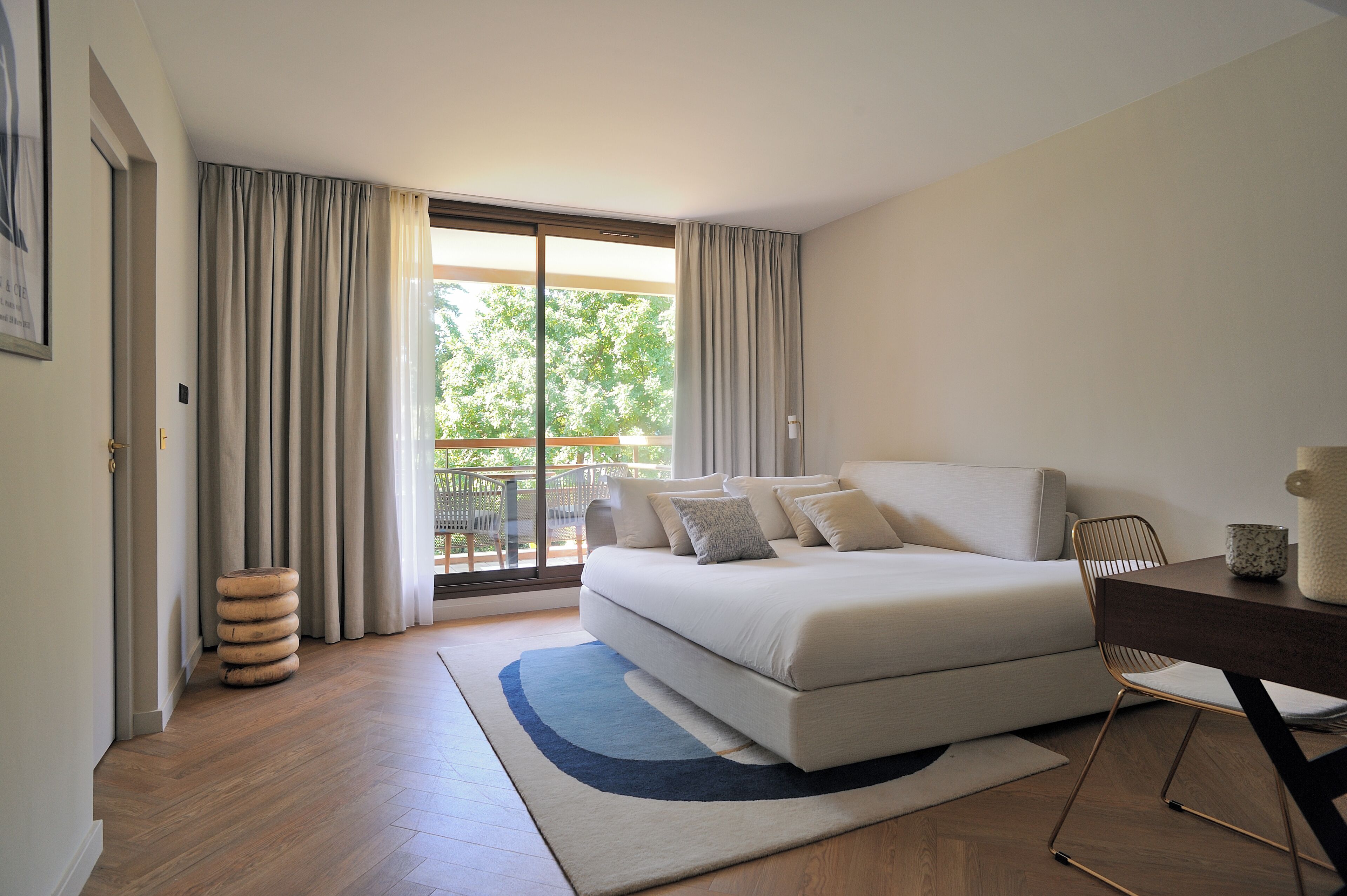 A bedroom with a large bed, a desk, and a view of the outdoors.