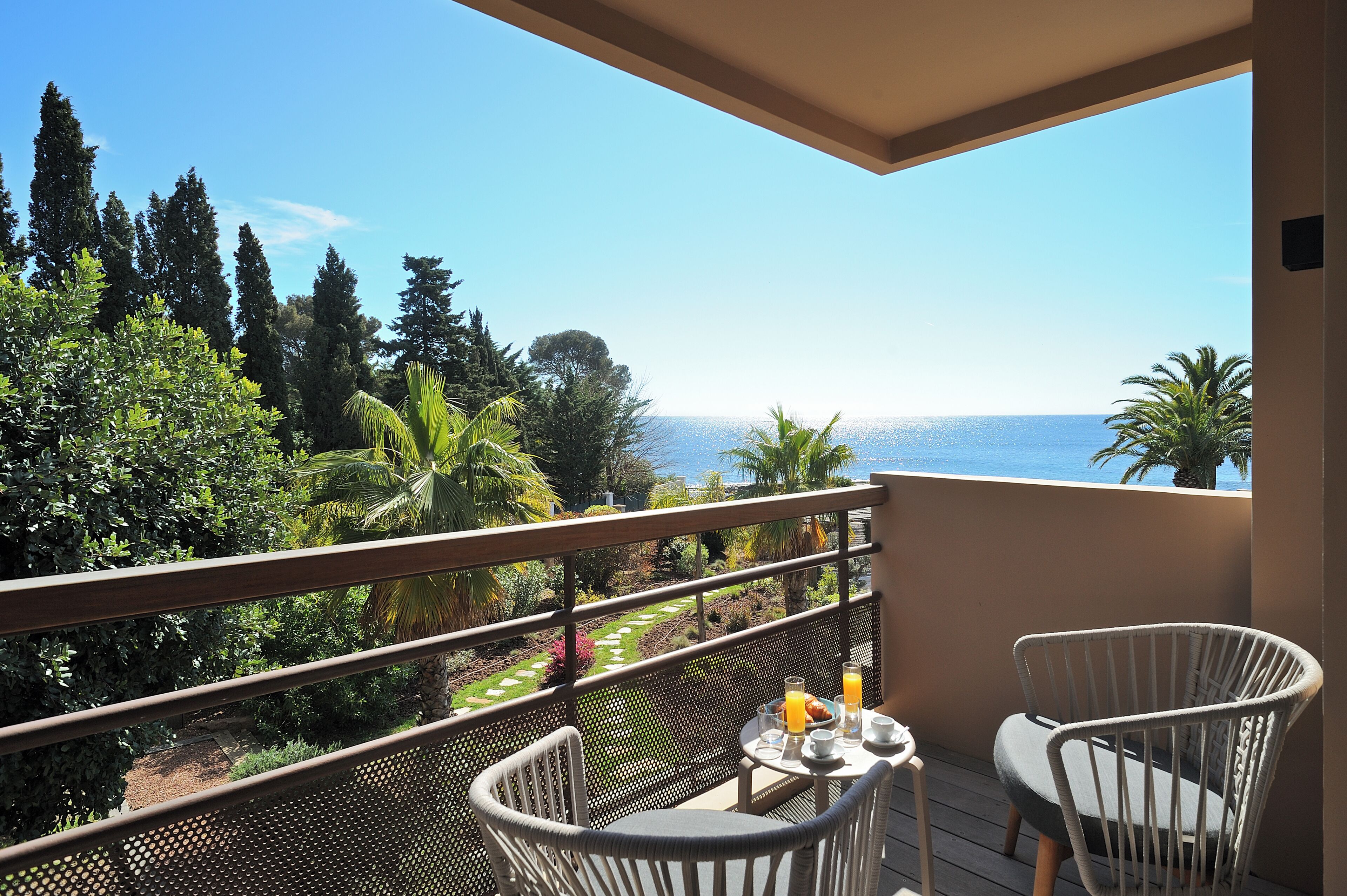 A balcony with a view of the sea, a table with breakfast items, and two wicker chairs.