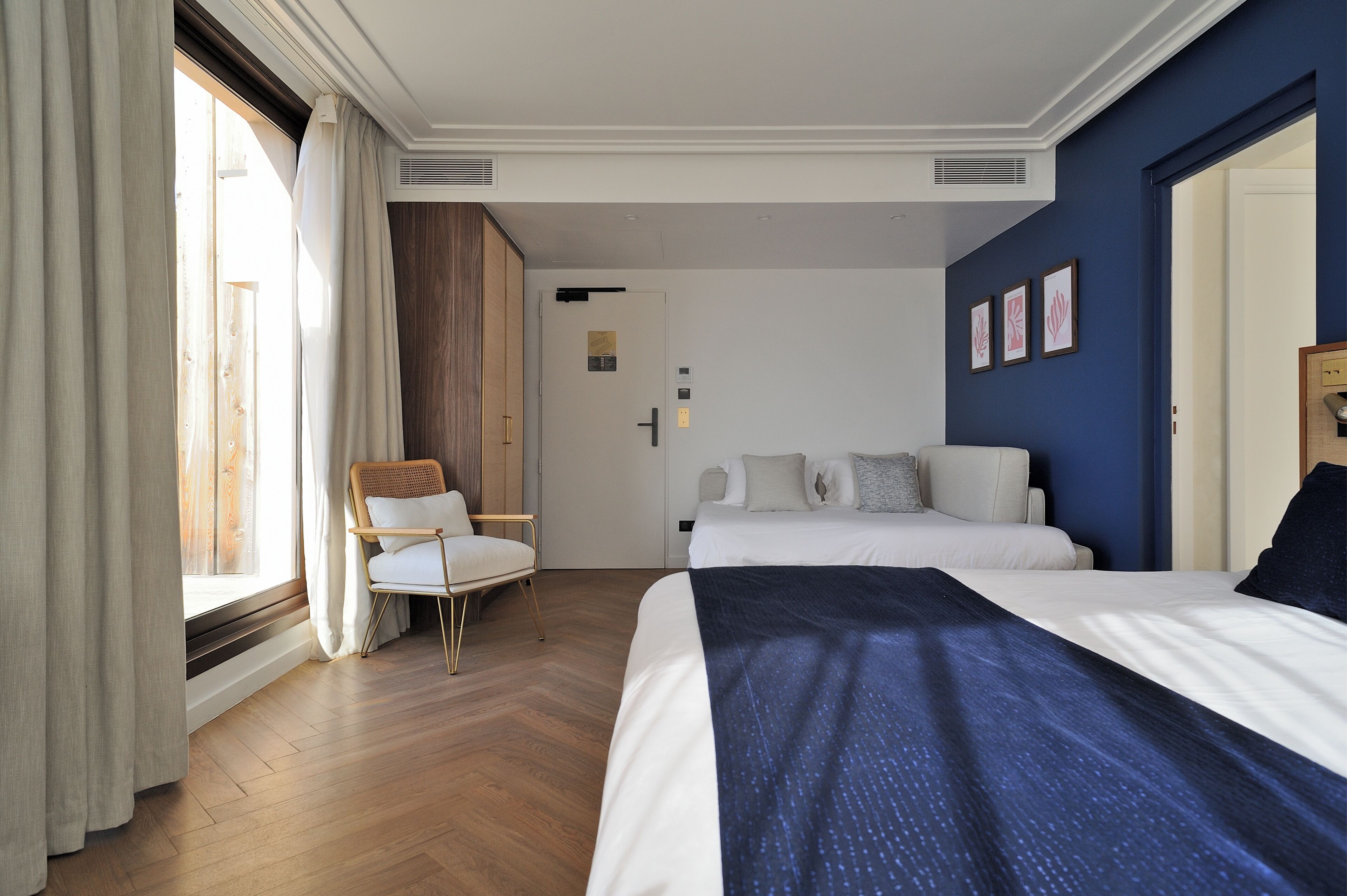 Una camera d'albergo con un letto, una sedia, una finestra con tende e una porta con ascensore.