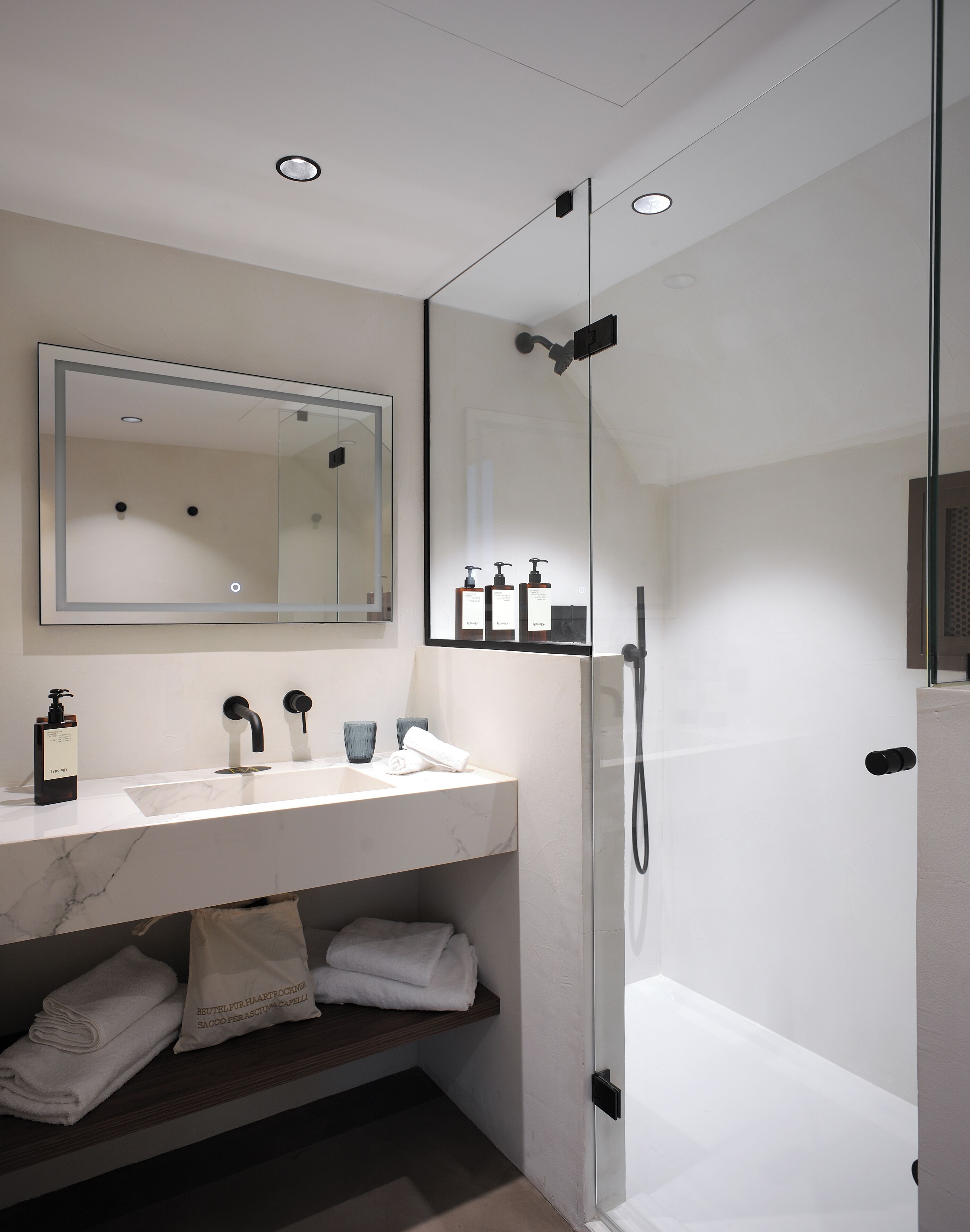 Un baño moderno con cabina de ducha de vidrio, lavamanos de mármol y un espejo grande.