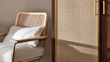 A room with a wooden floor, a wicker chair with a white cushion, and a wooden door with a textured panel.