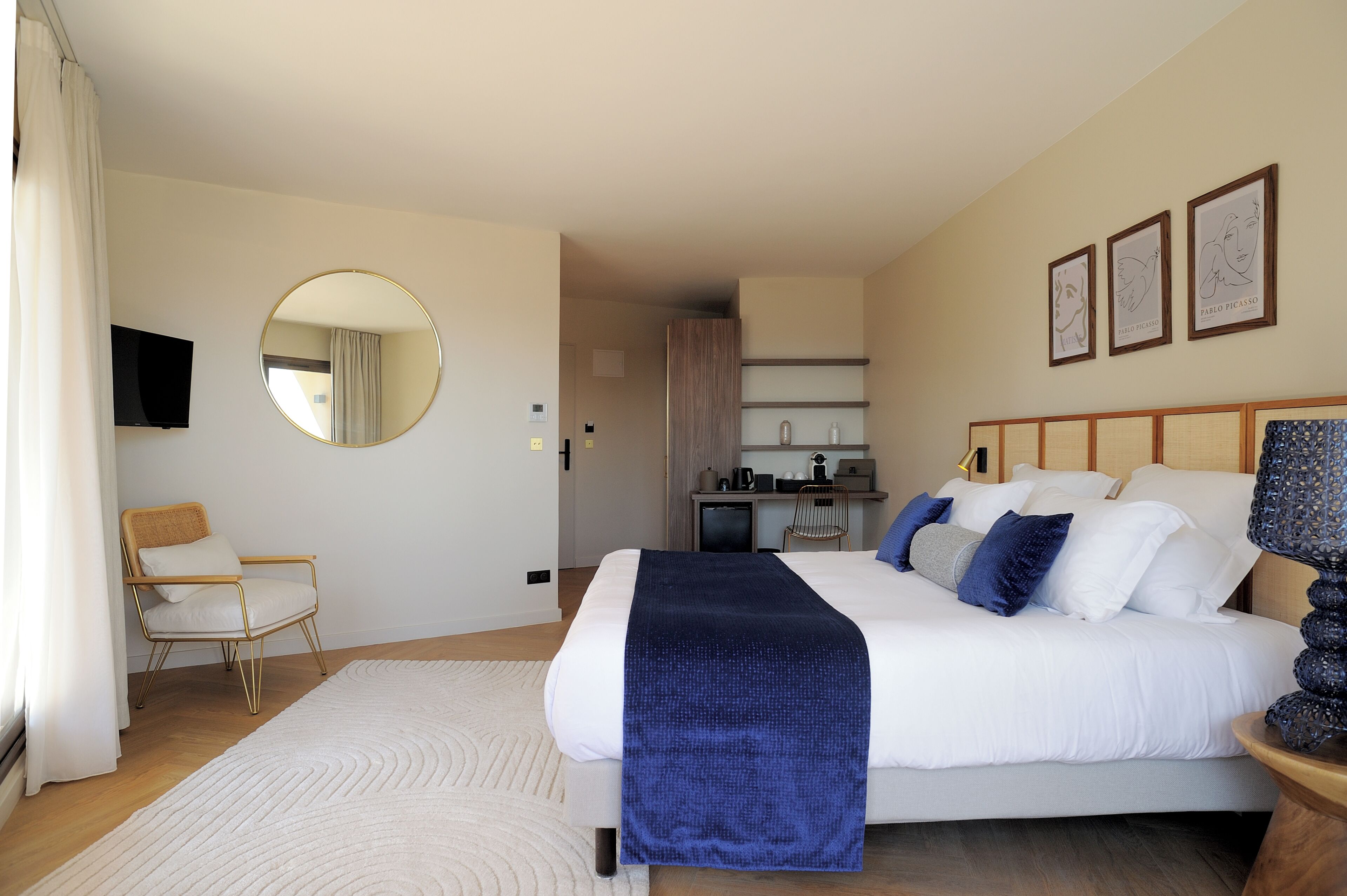 A bedroom with a bed, a round mirror, a chair, a television, and artwork on the wall.