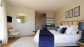 A bedroom with a bed, a round mirror, a chair, a television, and artwork on the wall.