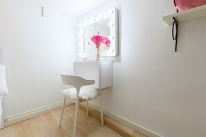 A white vanity with a mirror surrounded by lights, a white chair with a fluffy seat, and a small shelf with a pink object. - M Hor291 Moderno d Plex de 1 Dormitorio con Toda (Madrid)