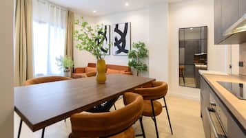 A modern kitchen with a wooden table and chairs, a built-in oven, and a large window with curtains.